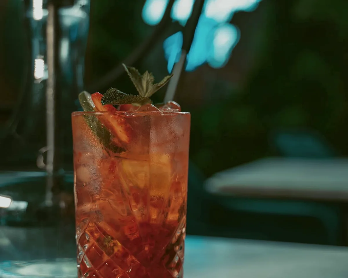 A fruit mocktail over ice in a cut-glass tumbler, with a shisha pipe and the garden behind it