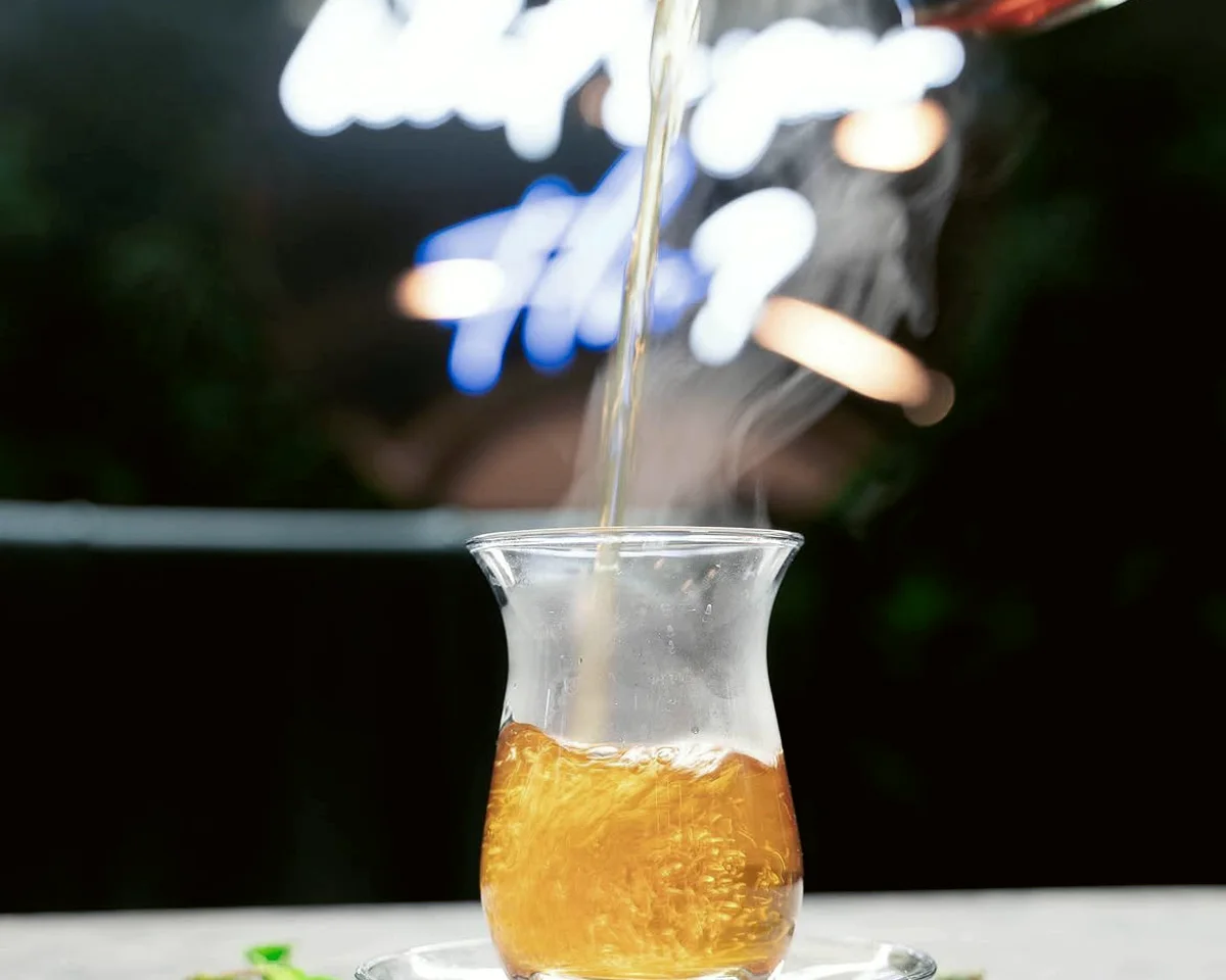 Mint tea being poured into a Turkish tea glass under the lounge neon