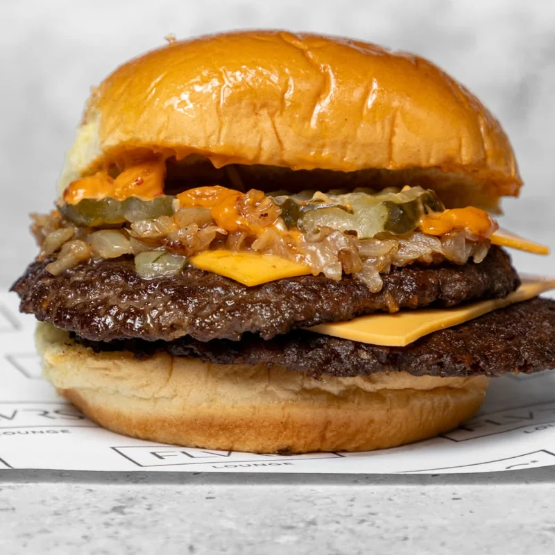 Two stacked beef patties with melted cheese, gherkins and caramelised onions in a toasted potato bun